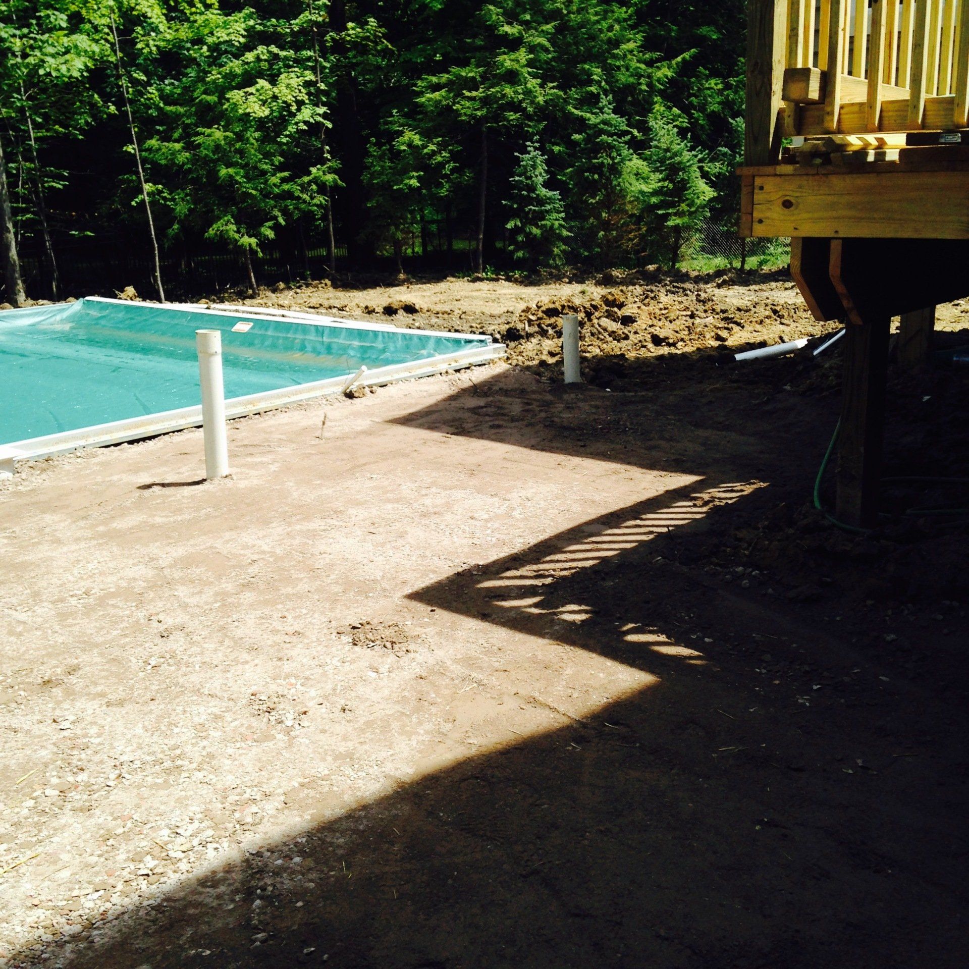 Construction site beside a turquoise pool, with a wooden structure casting a large shadow on dirt ground.