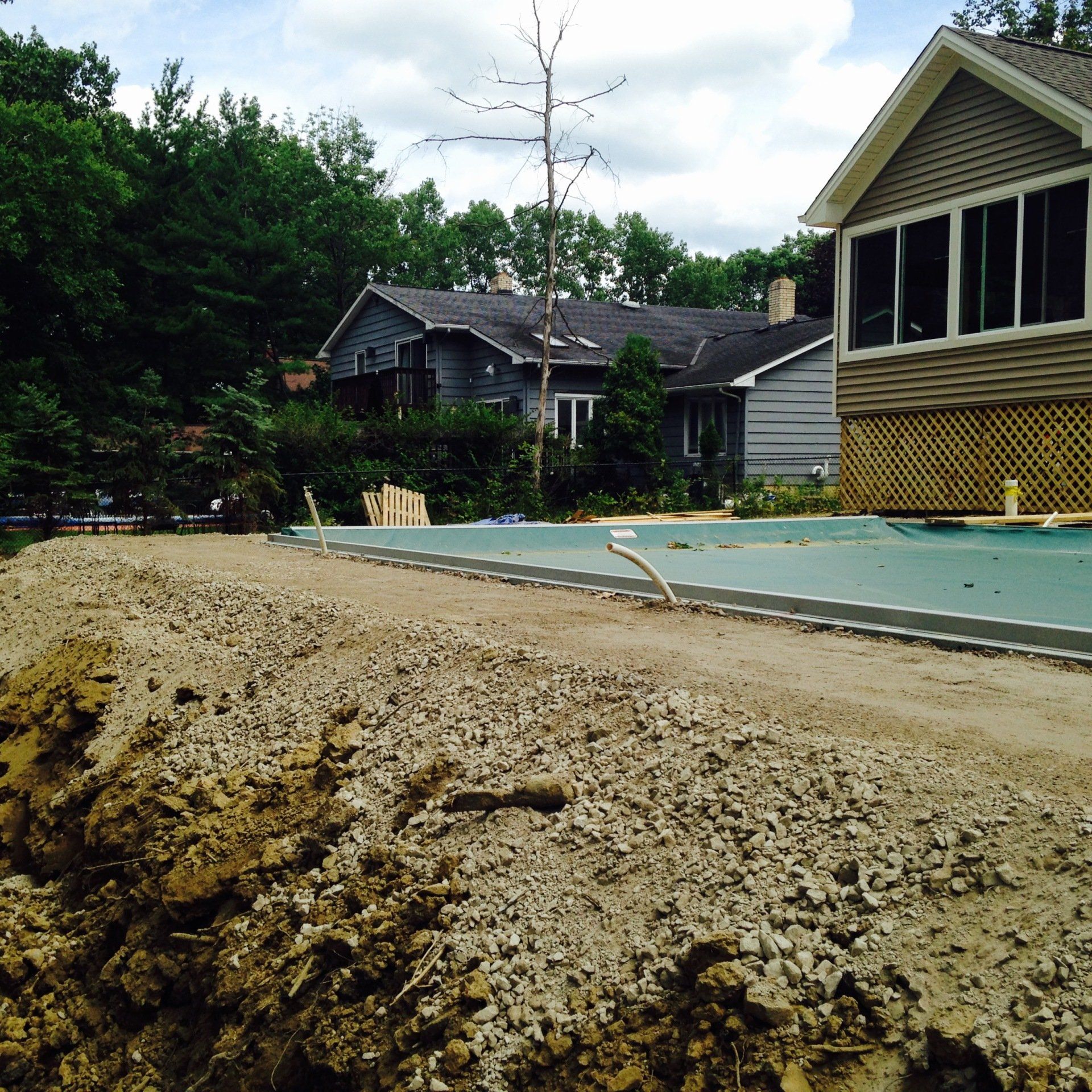 Mound of dirt beside a newly poured concrete slab at a house under construction, with trees and homes in background