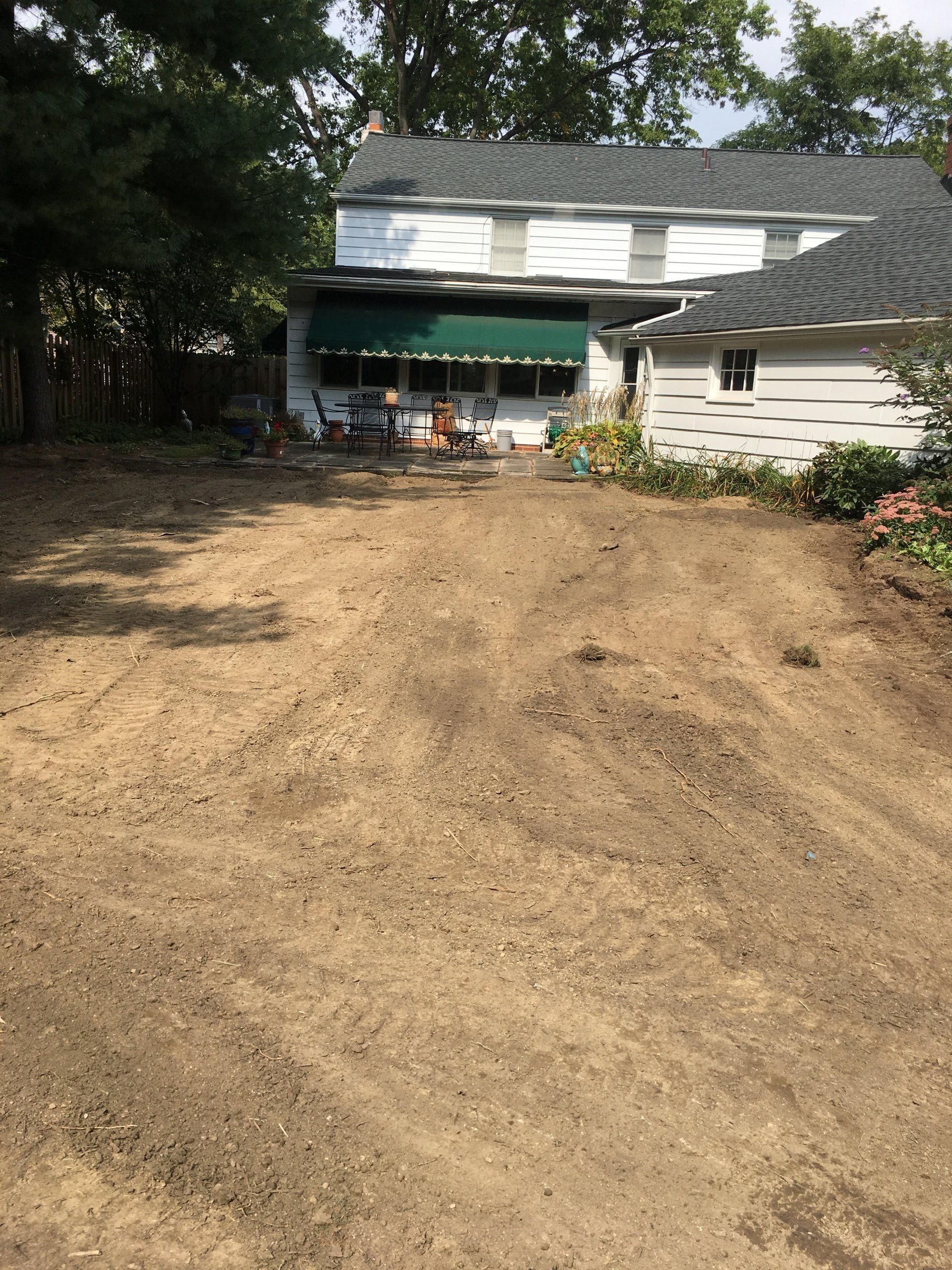 Dirt backyard with a house, green awning, and chairs on a porch under trees