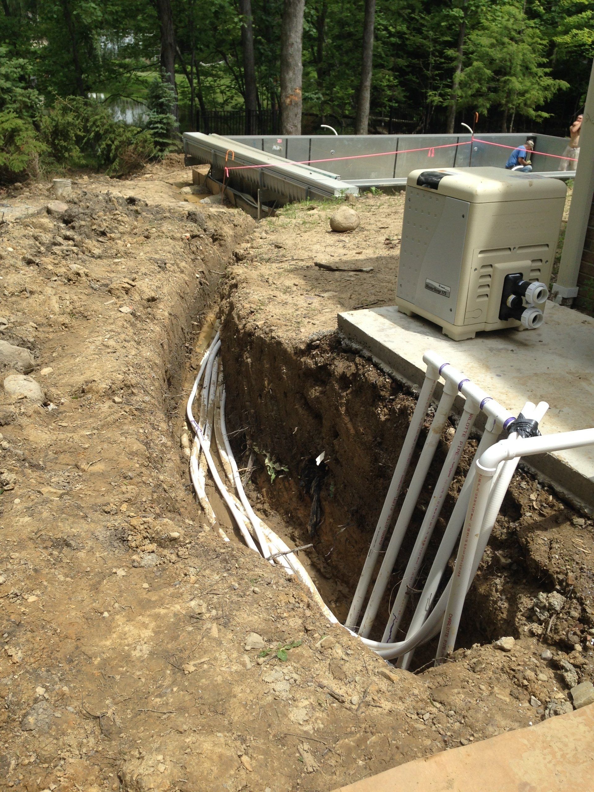 Open trench with exposed utility pipes beside a roadside construction site and concrete slab