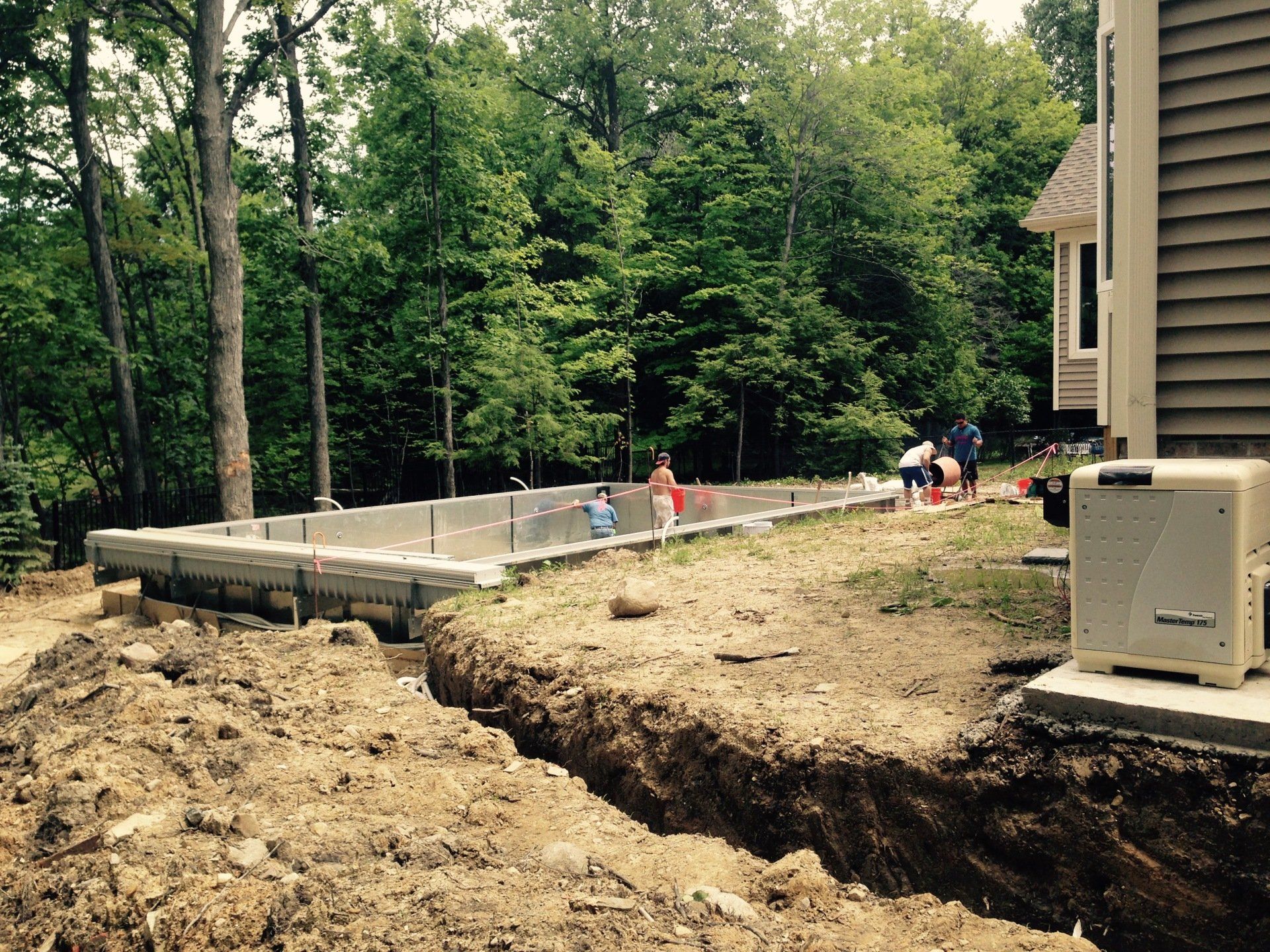 Backyard construction site with a partially built concrete foundation and workers near a house