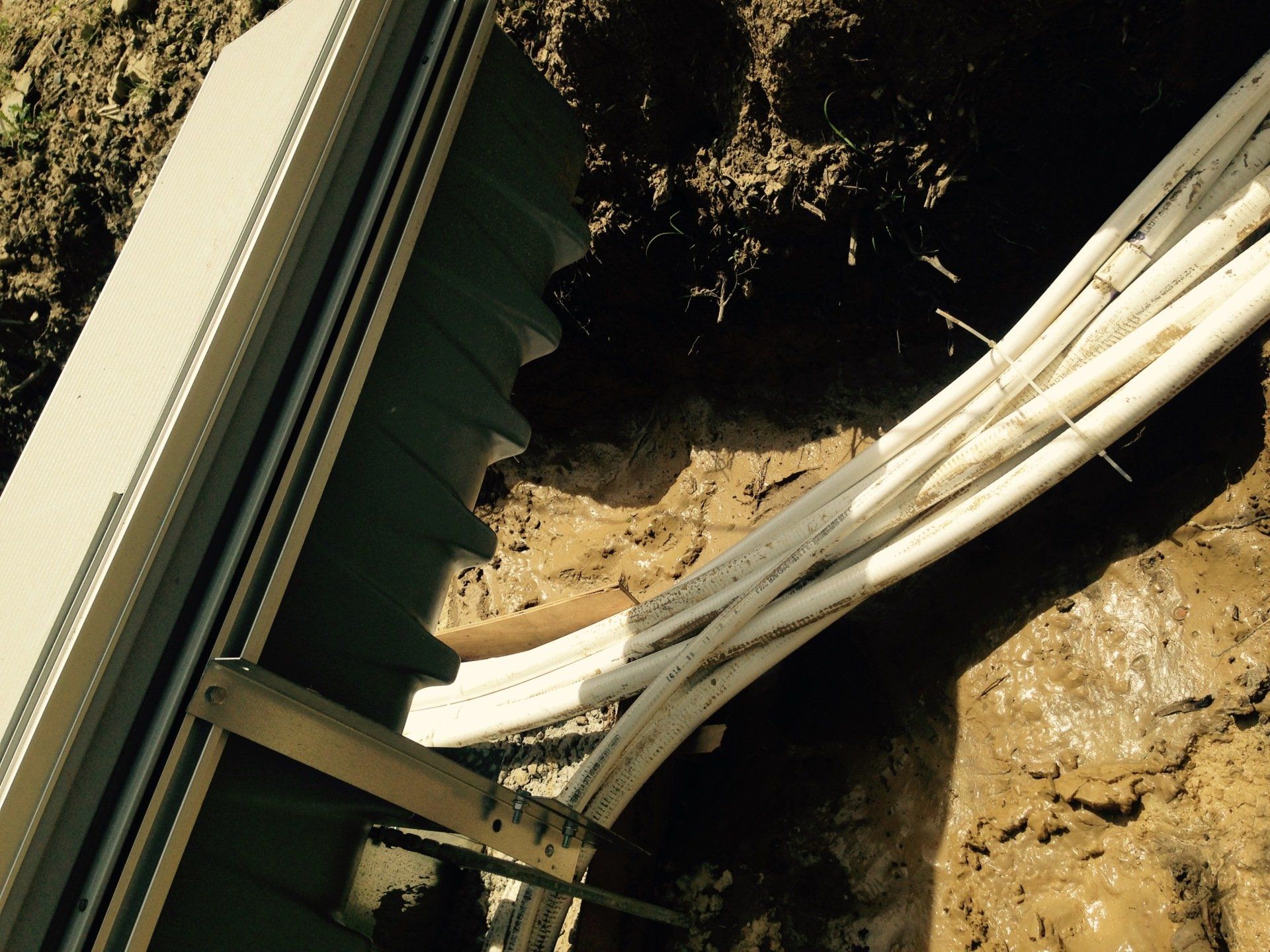 Broken white pipes lying in muddy ground beside a building wall