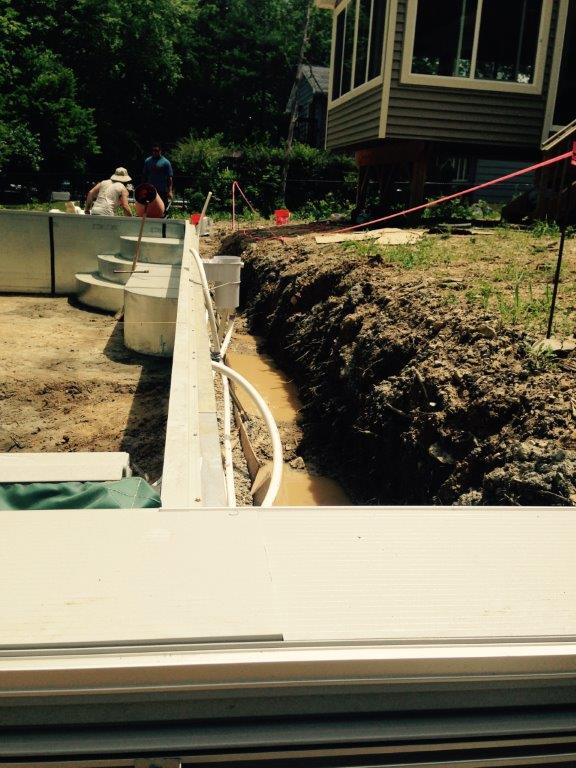 Construction site with a concrete foundation wall, trench, dirt piles, and a worker in the background