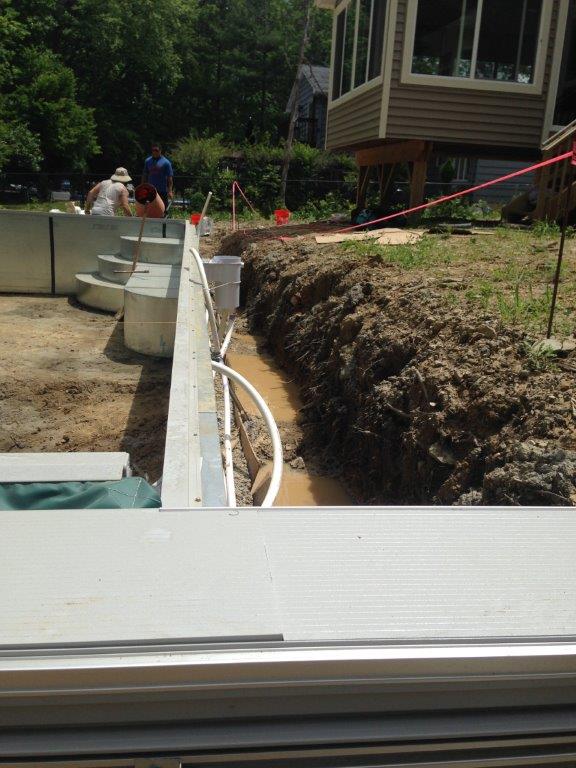 Construction site with concrete foundation walls, trenching, and workers near a house foundation
