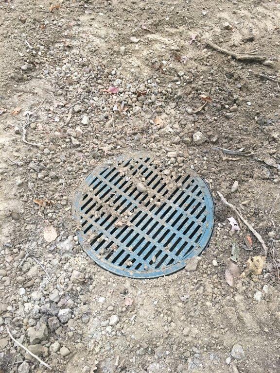 Round metal drain grate set in rough dirt ground.