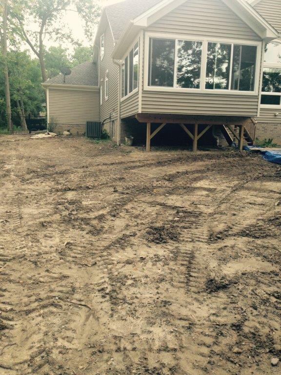 House on dirt lot with exposed foundation and screened porch, surrounded by trees