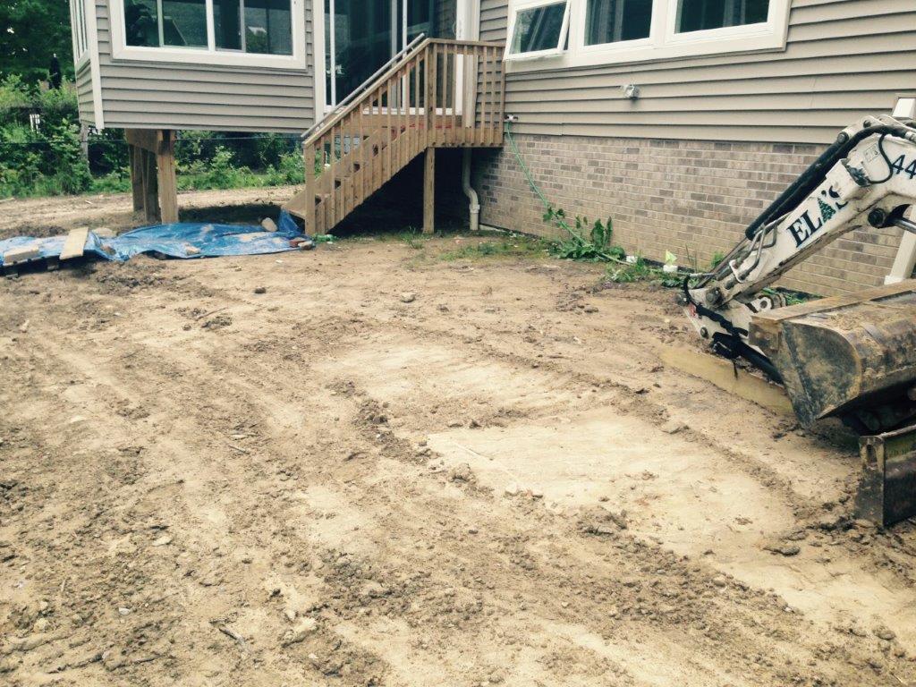 Dirt-filled yard under construction beside a house, with a skid steer and porch stairs visible.