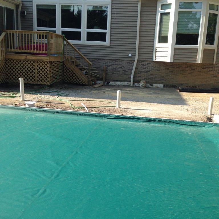 Backyard pool under construction beside a house, with turquoise liner and deck posts.