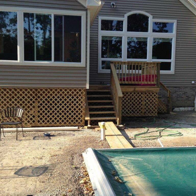 Backyard deck with stairs, lattice skirting, and a swimming pool in the foreground.