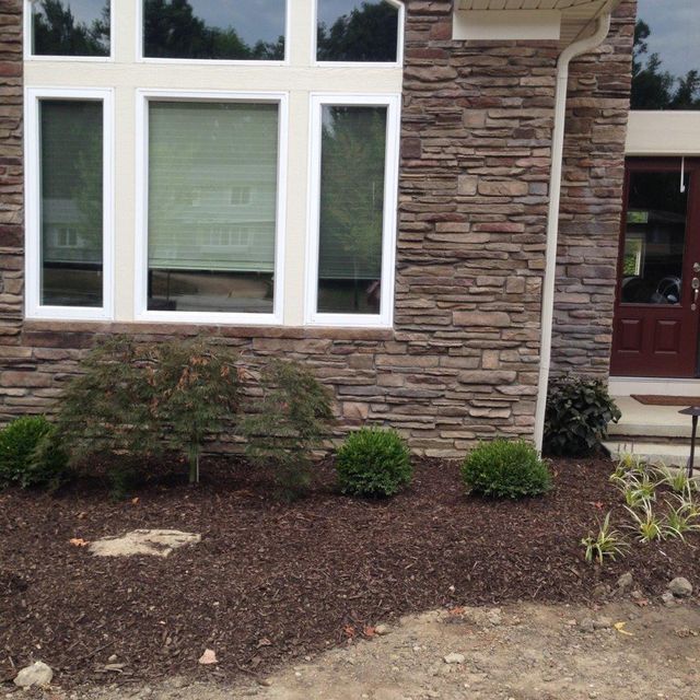 Front of a house with stone siding, large white-framed windows, and a mulched garden bed.