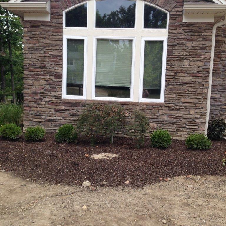 Stone house exterior with a large white-trimmed window and landscaped mulch bed
