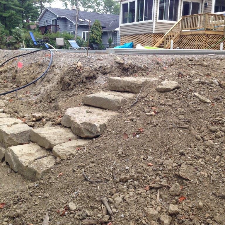 Backyard dirt slope with stone steps leading up to a house under construction
