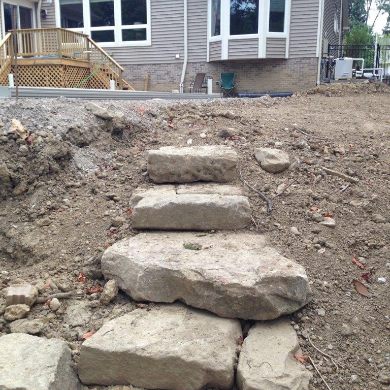 Rough stone steps leading up a dirt slope to a house under construction