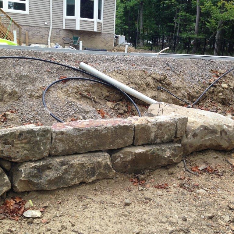 Stone retaining wall with exposed black cable and white pipe at a construction site