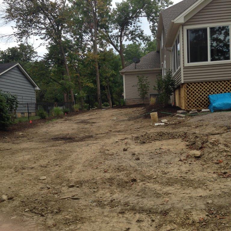 Dirt-covered backyard beside a house, with trees and a small outbuilding in the background.