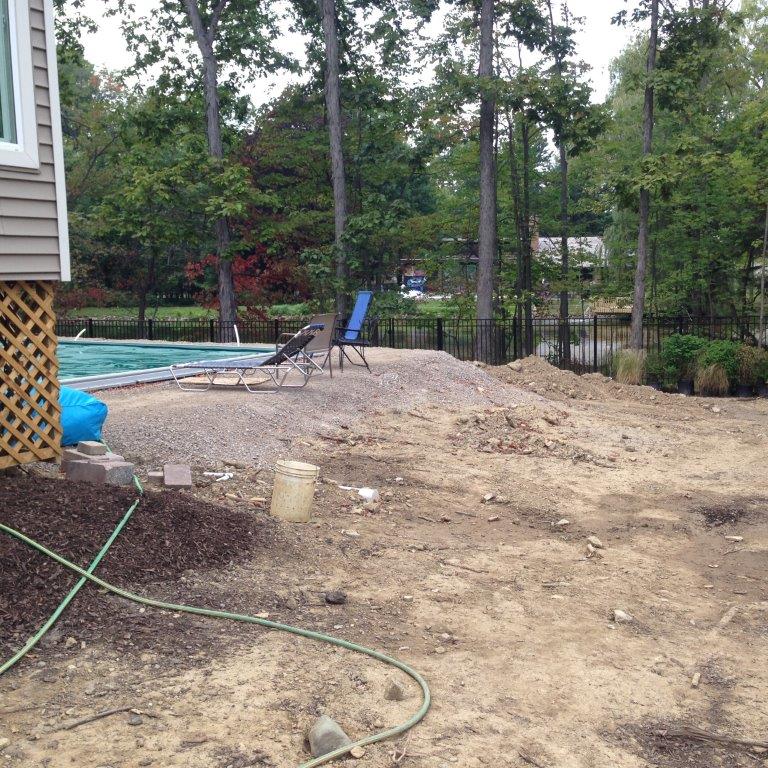 Backyard with a swimming pool, lounge chair, dirt mound, and trees beside a house