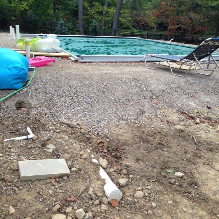 A gravel pool area with a swimming pool, lounge chair, and scattered debris in the foreground.