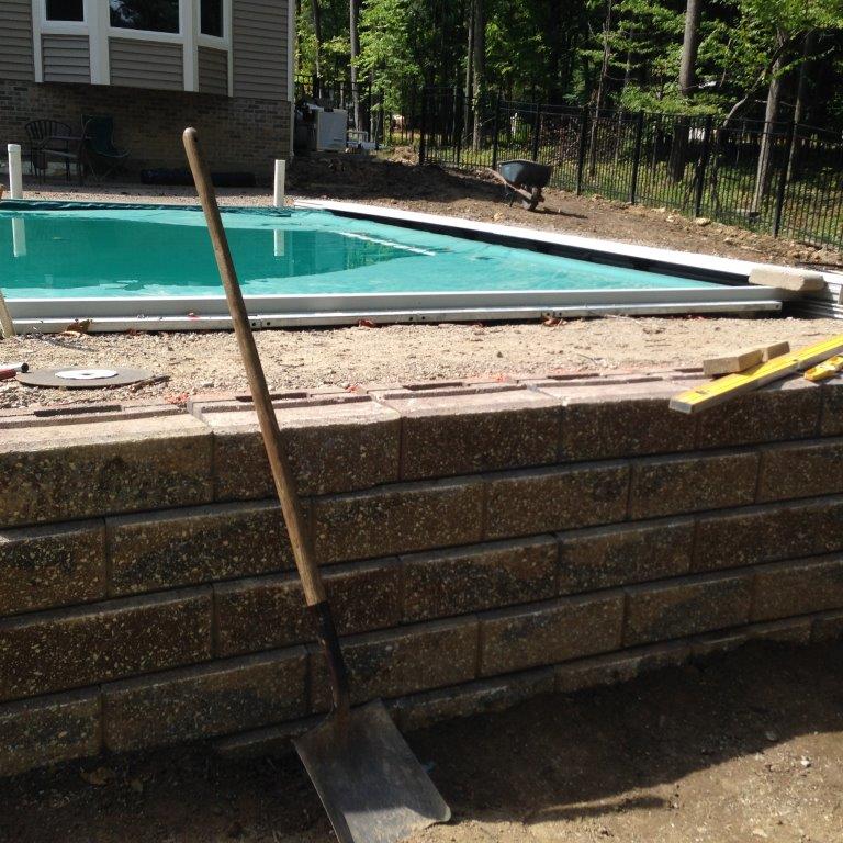 Shovel leaning against a stone pool wall beside an in-ground swimming pool under construction