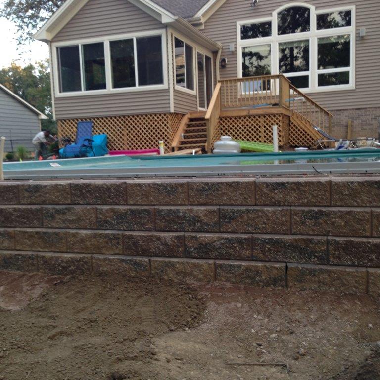 Backyard house with a raised deck, stone retaining wall, and a dirt foreground under construction