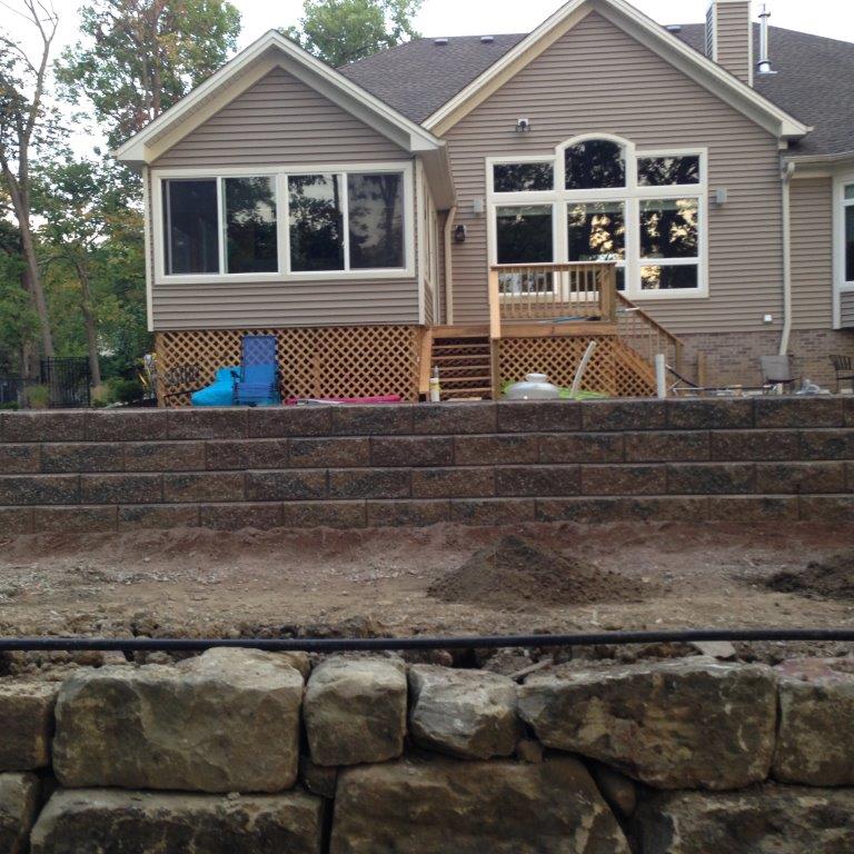 House with new stone retaining wall and unfinished backyard landscaping under construction