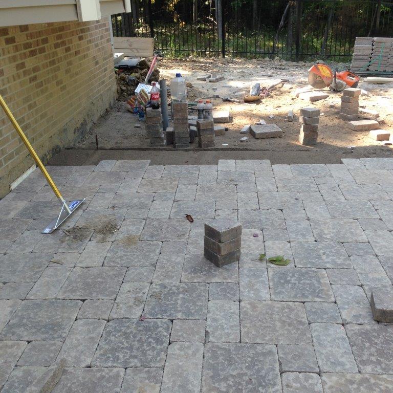 Backyard patio under construction with stacked pavers, tools, and unfinished ground area