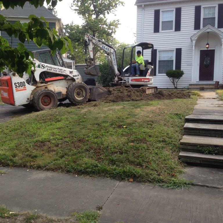 Construction crew using a skid steer and excavator to grade a front yard beside a white house