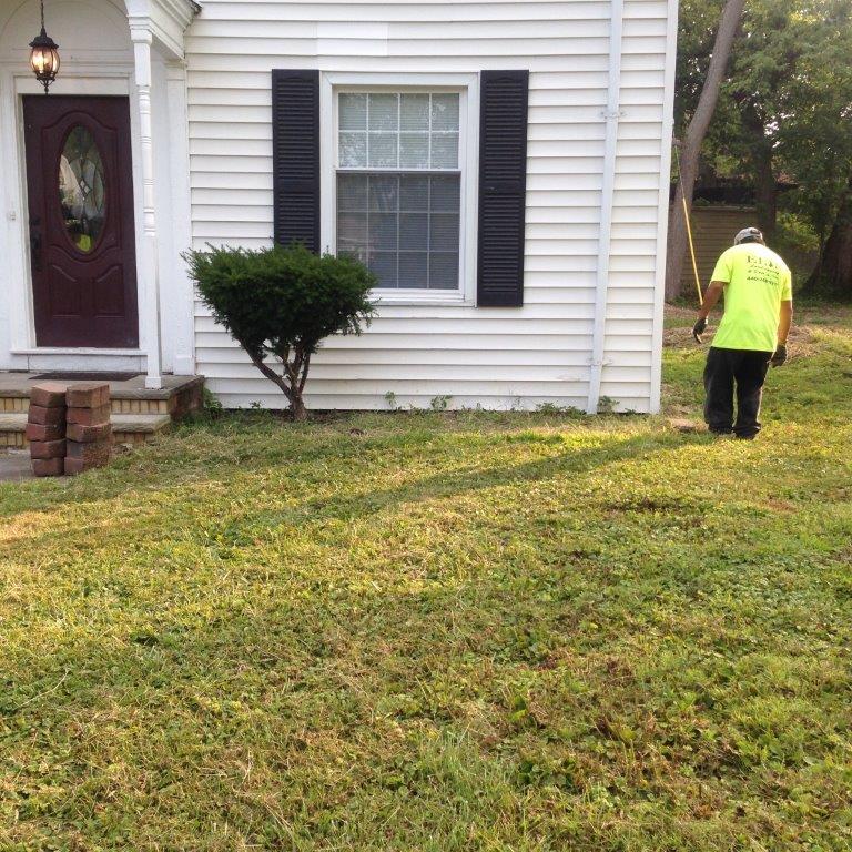 Worker mowing grass beside a white house with a maroon door and window
