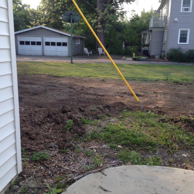 Backyard dirt patch with a yellow utility pole, garage in the background, and part of a concrete patio.