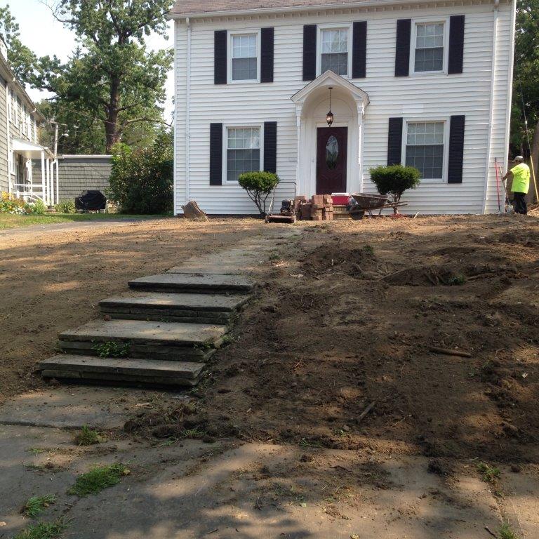 Two-story white house with black shutters and a newly graded front yard with steps leading up to the entrance