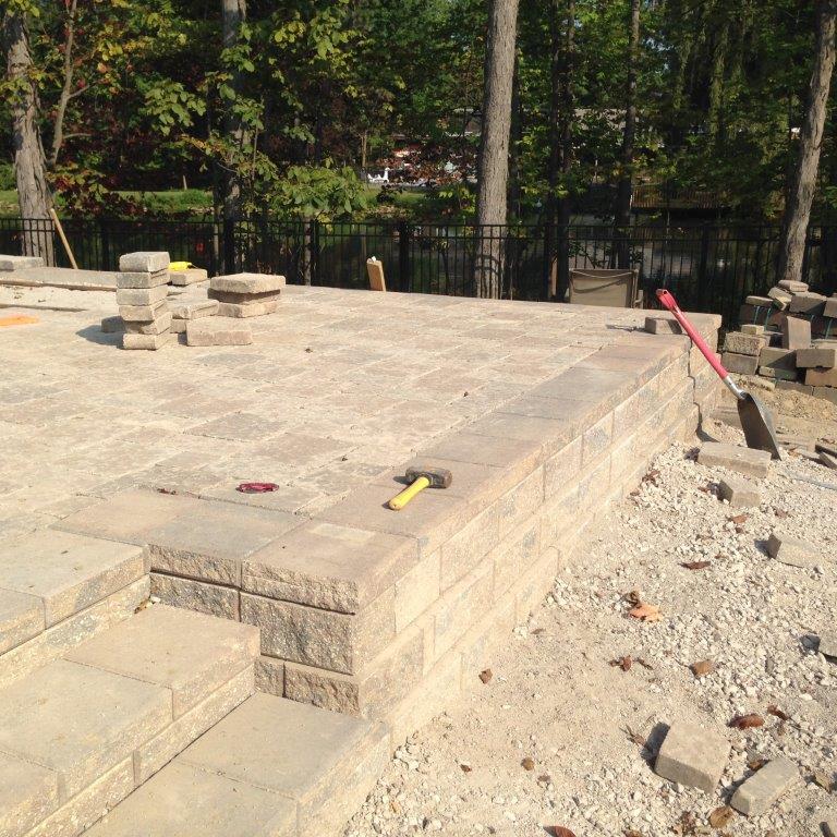 Concrete foundation under construction with stacked blocks, a hammer, and a shovel on a sunny outdoor site.
