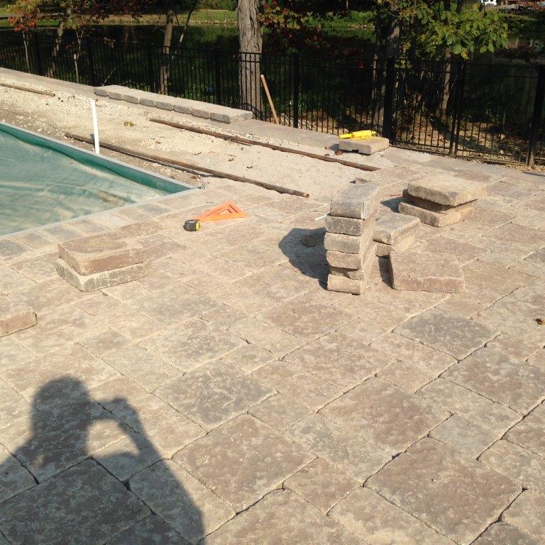 Stone patio beside a swimming pool with stacked pavers and a shadow in the foreground