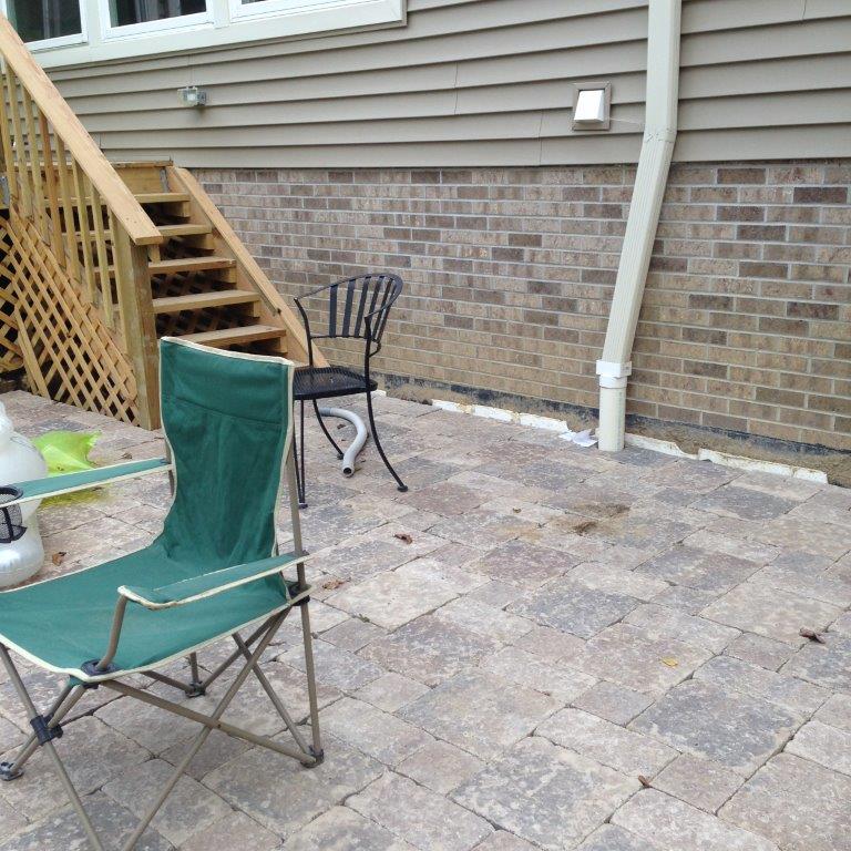 Backyard patio with stone pavers, two folding chairs, stairs, and a brick house wall