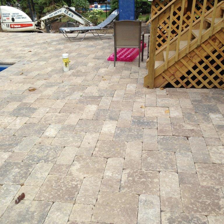 Stone patio with a small drink, lounge chair, and wooden lattice fence beside a pool area