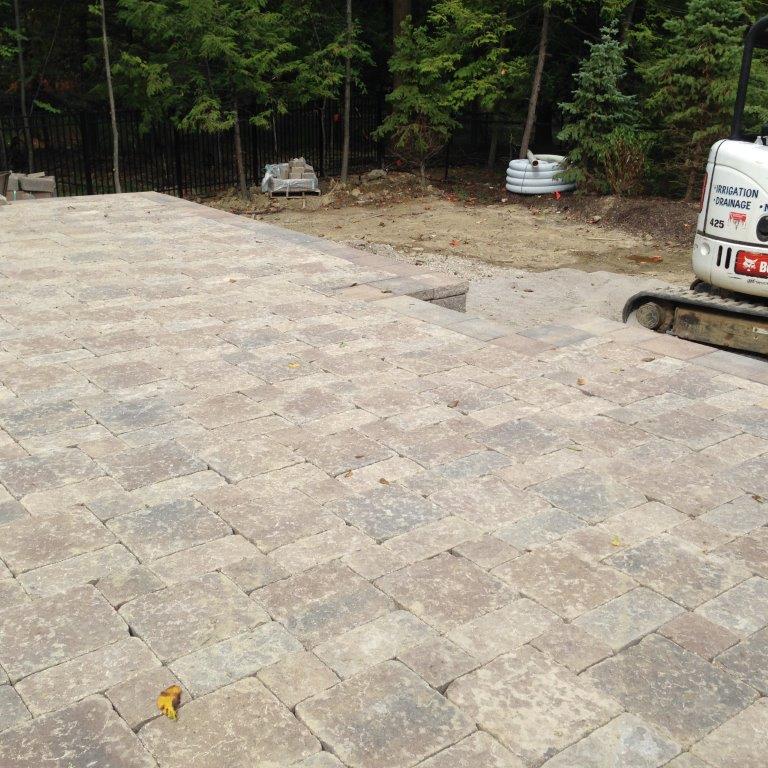 Stone-paved driveway under construction beside a wooded area, with a work van at right