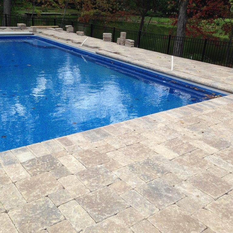 Blue swimming pool beside a beige stone deck and black fence outdoors