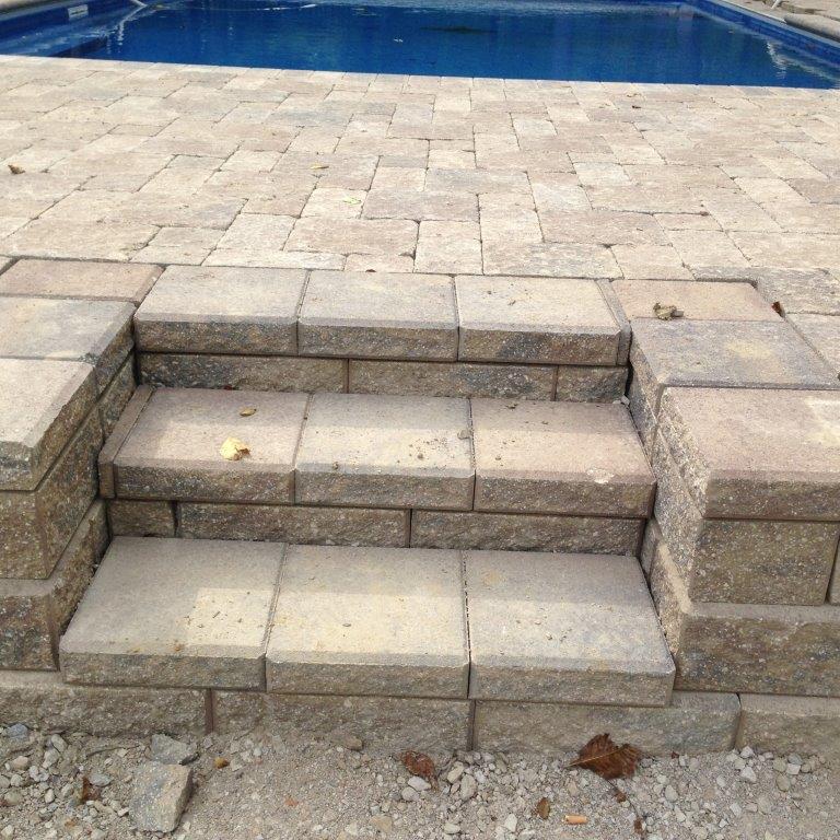 Stone steps leading to a blue swimming pool on a paved patio
