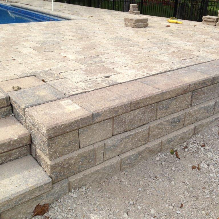 Stone patio with a raised retaining wall and steps on the left, viewed from a corner.