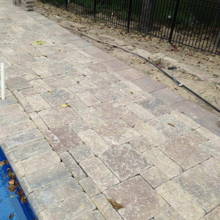 Stone-paved sidewalk beside a black metal fence and a blue curb edge