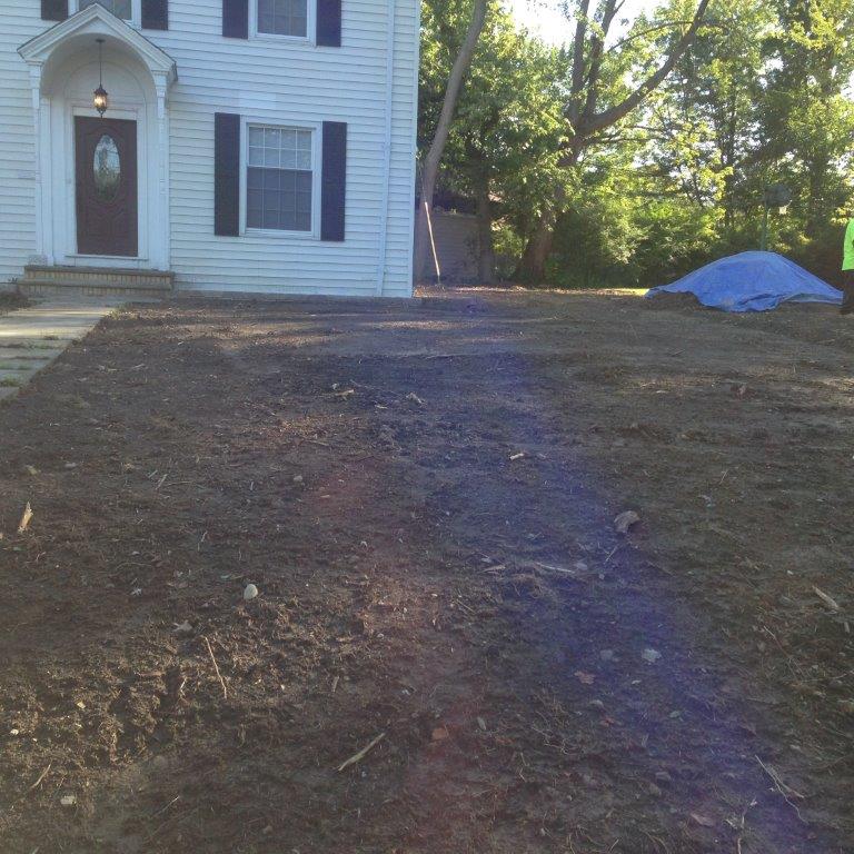 House front with bare yard and a blue tarp near trees in the background