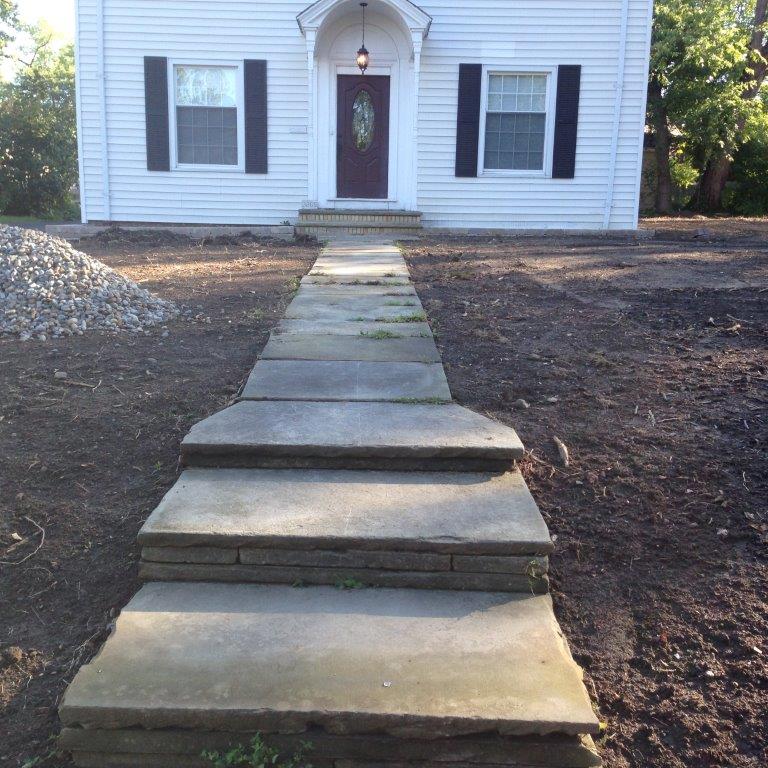 Steep concrete walkway with steps leading to a white house with dark shutters and front door