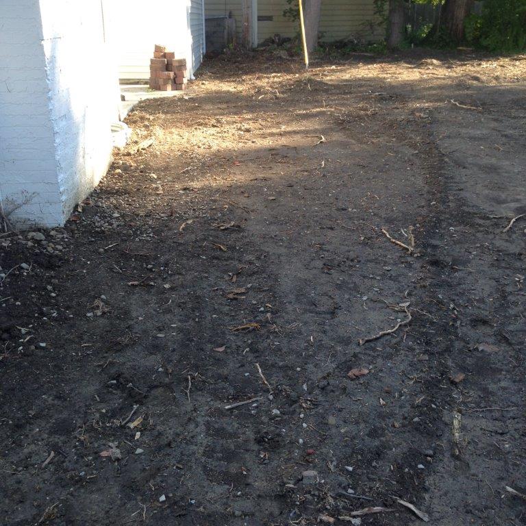 Dirt driveway beside a white building, with tire tracks and trees in the background.