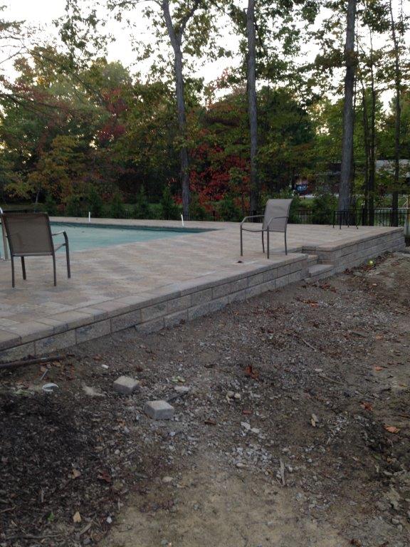 Backyard patio with a small pool, chairs, and trees, beside a bare dirt slope