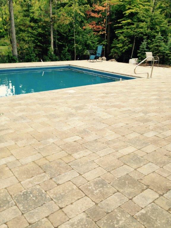 Swimming pool beside a beige stone patio with trees in the background