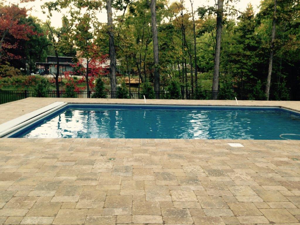 Rectangular backyard swimming pool with blue water beside a stone patio and trees beyond