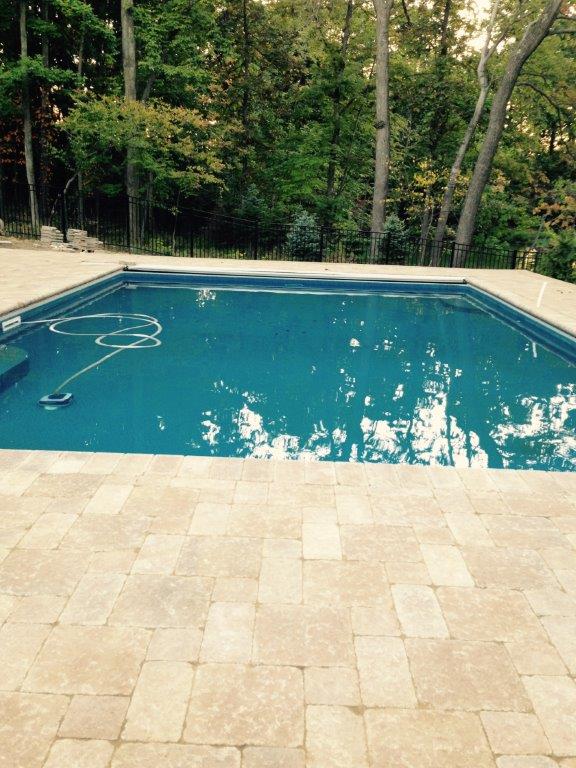 Backyard swimming pool with blue water, stone patio, and surrounding trees