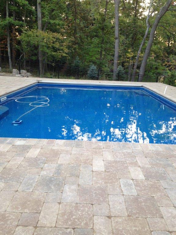 Blue swimming pool beside a stone patio, with trees reflected in the water.