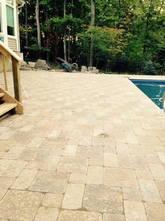 Stone patio beside a swimming pool with trees and a wooden deck in the background