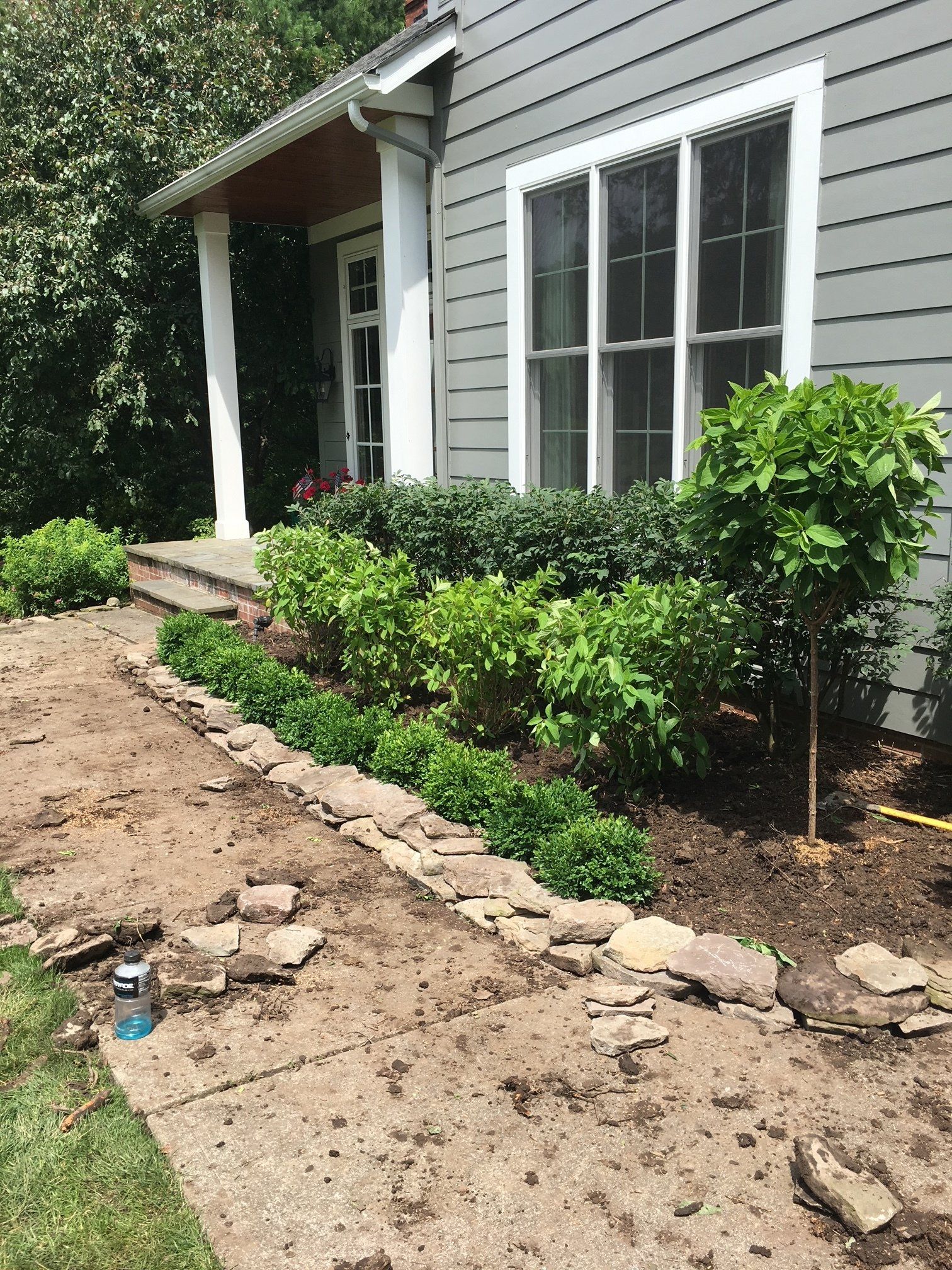 Front yard of a house with shrubs, a dirt path, and white-framed windows and porch columns.