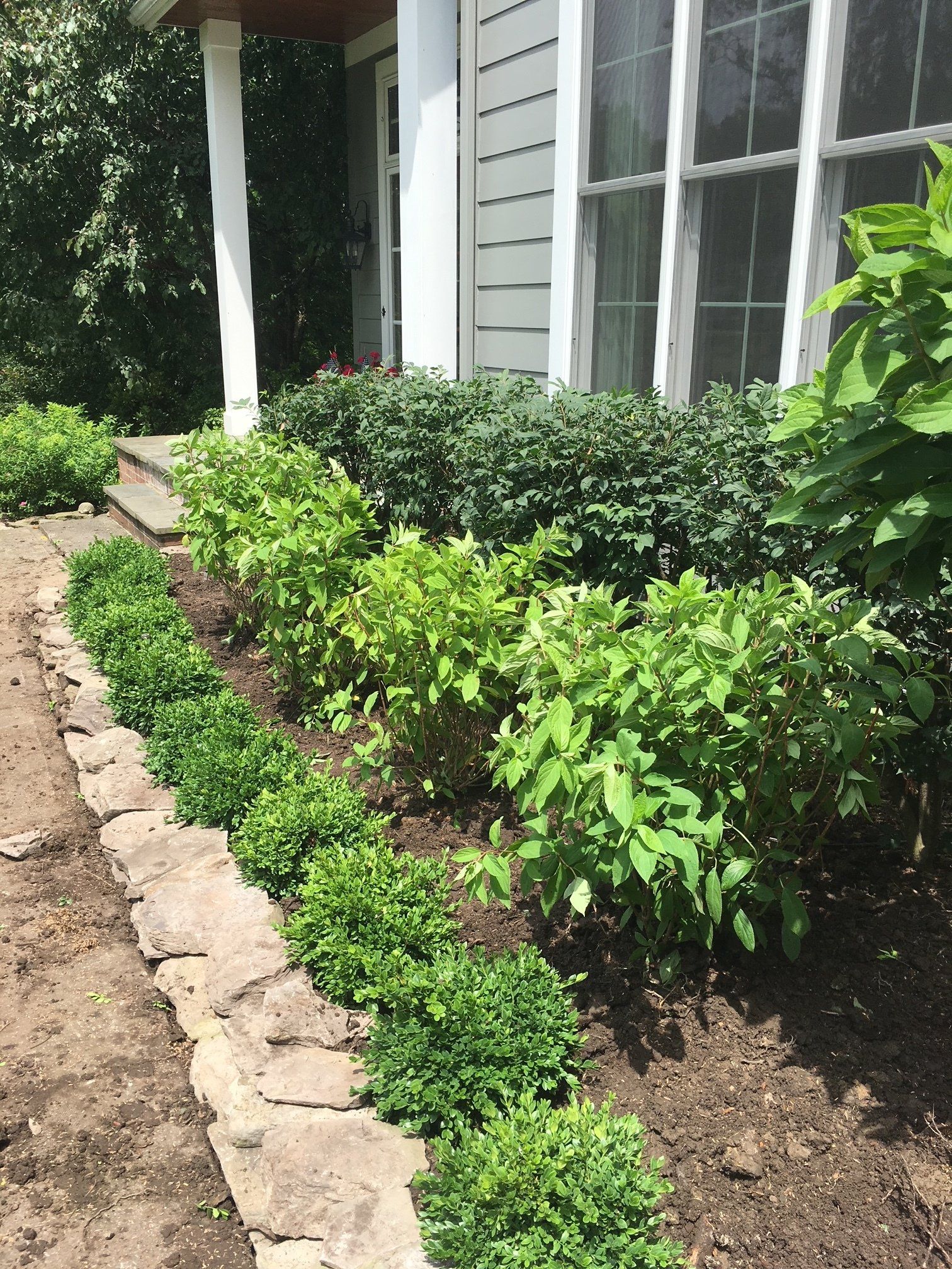 Front yard garden bed with shrubs and stone edging beside a house porch