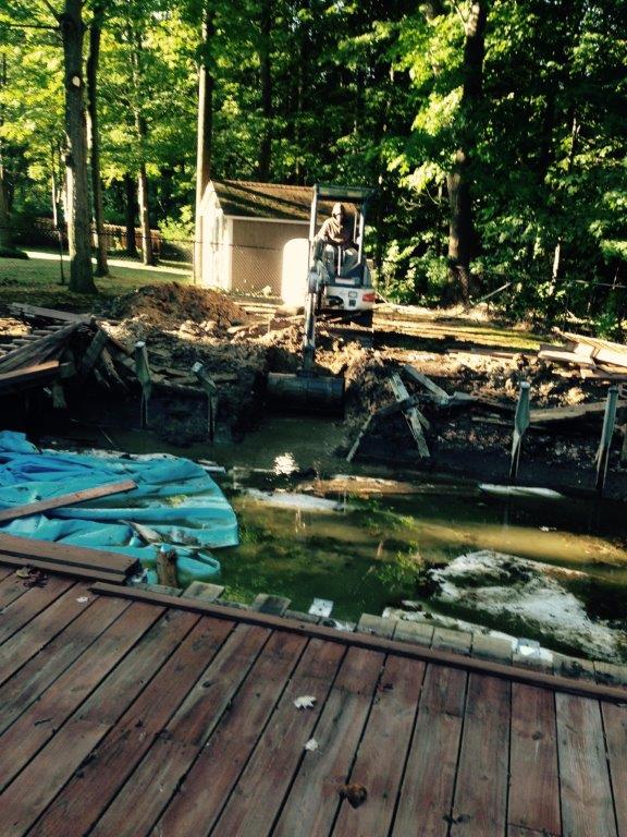Damaged lakeside dock with debris, a small shed, and trees in the background